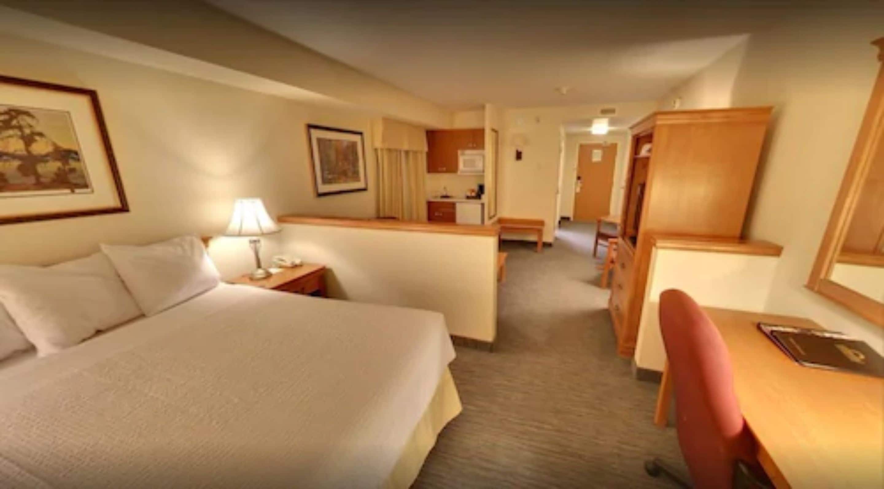 A hotel room with a large bed, a desk, a chair, and a small kitchenette.