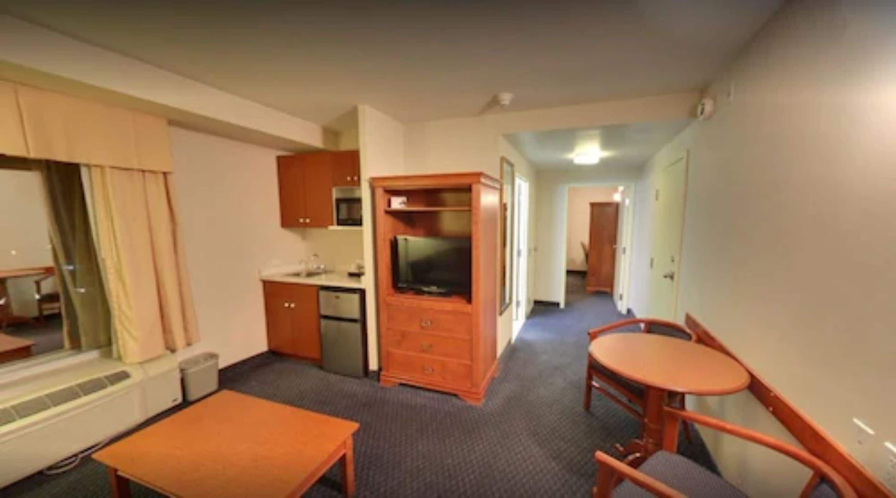 A compact hotel room with a kitchenette, a dining area, and a television.