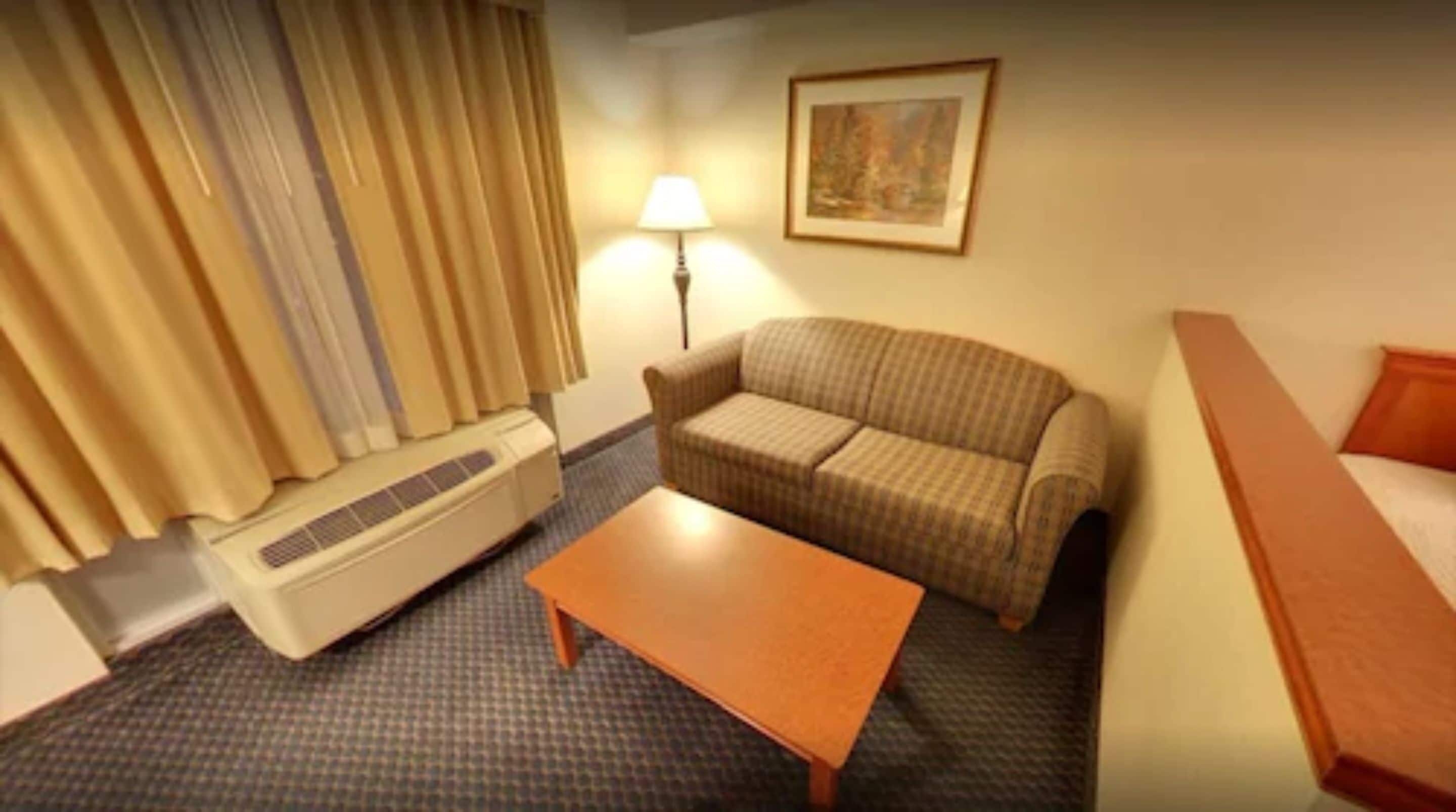 Quarto de hotel com sofá, mesa pequena, luminária e aquecedor.