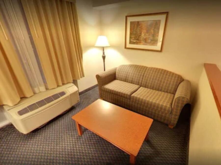 A hotel room with a sofa, a small table, a lamp, and a heater.