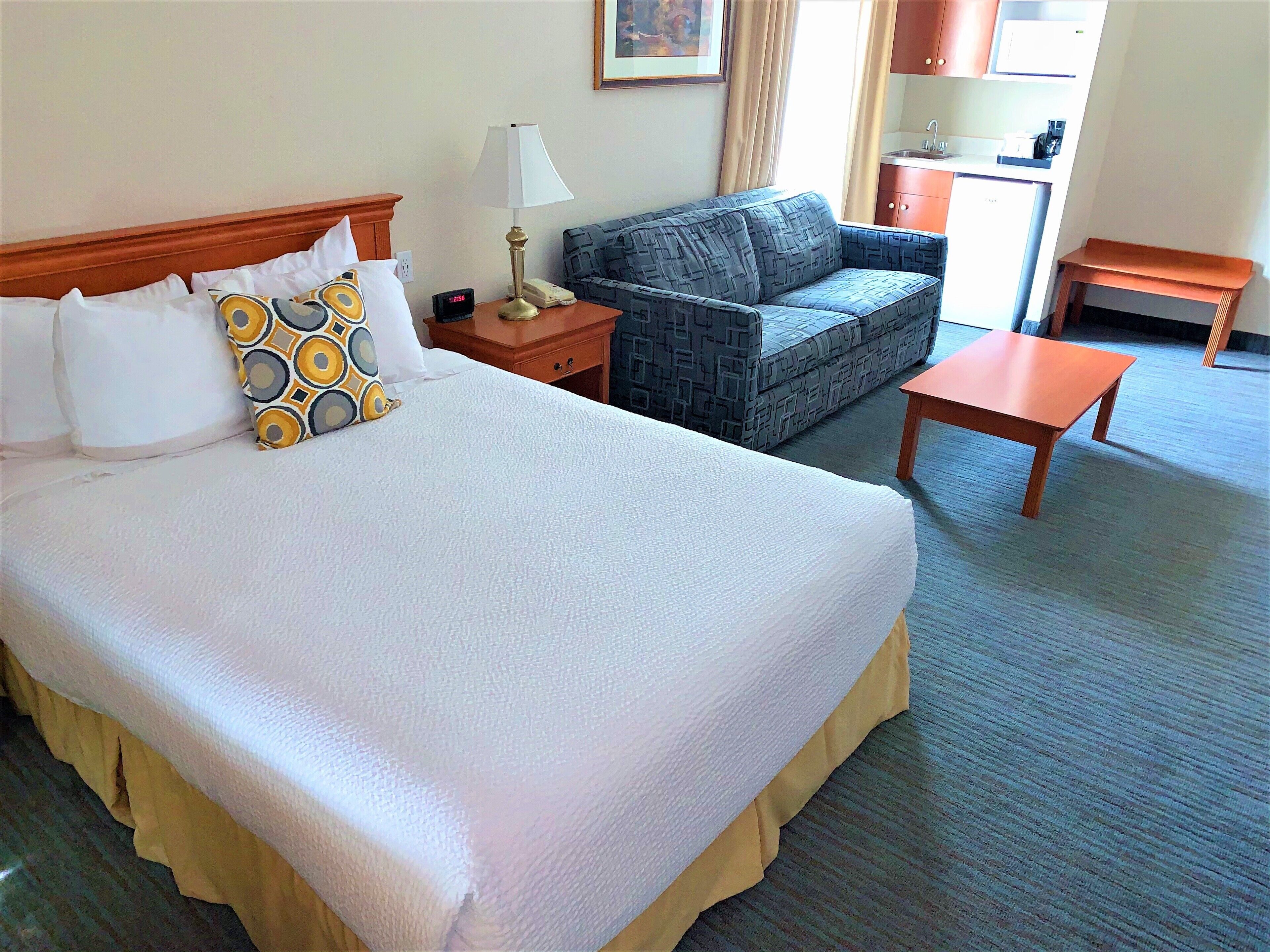 A hotel room with a large bed, a sofa, a small table, and a nightstand with a lamp and phone.