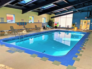 An indoor swimming pool with clear blue water, surrounded by lounge chairs and a tiled floor.