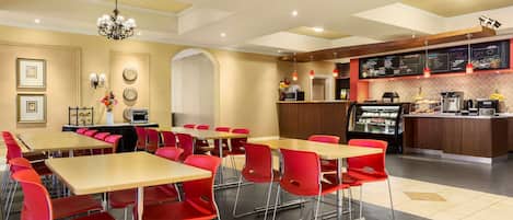 A modern dining area with red chairs and wooden tables, a coffee station, and a menu board.