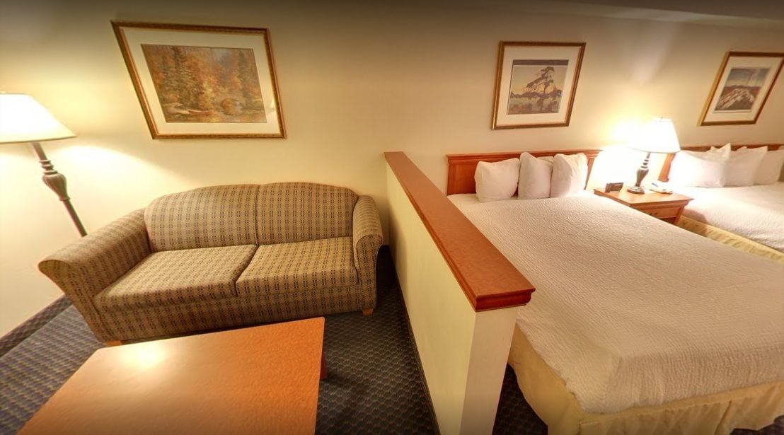 Una habitación de hotel con una cama individual, un sofá, una mesita y dos lámparas.