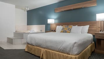A hotel room with a large bed, a wooden headboard, a bedside table with a lamp, a nightstand, and a built-in shelf above the bed.
