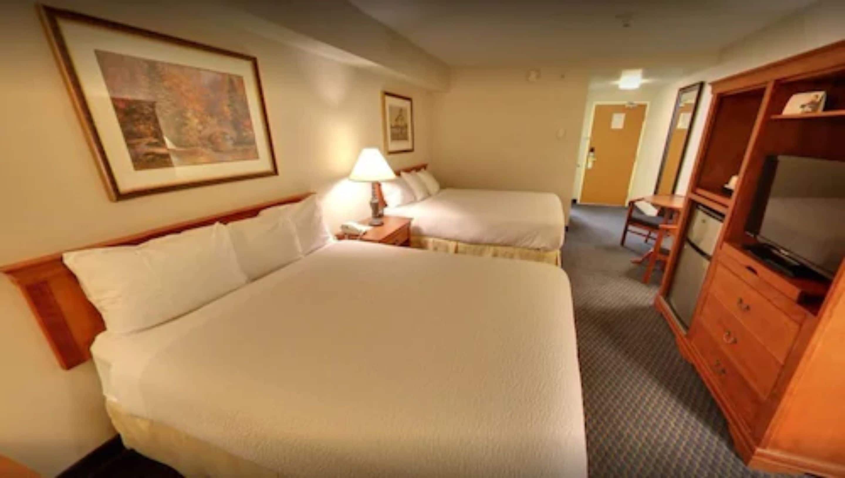A hotel room with two beds, a desk, a chair, a television, and a painting on the wall.