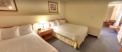 A hotel room with two beds, a nightstand with a lamp, and a small desk with a chair.