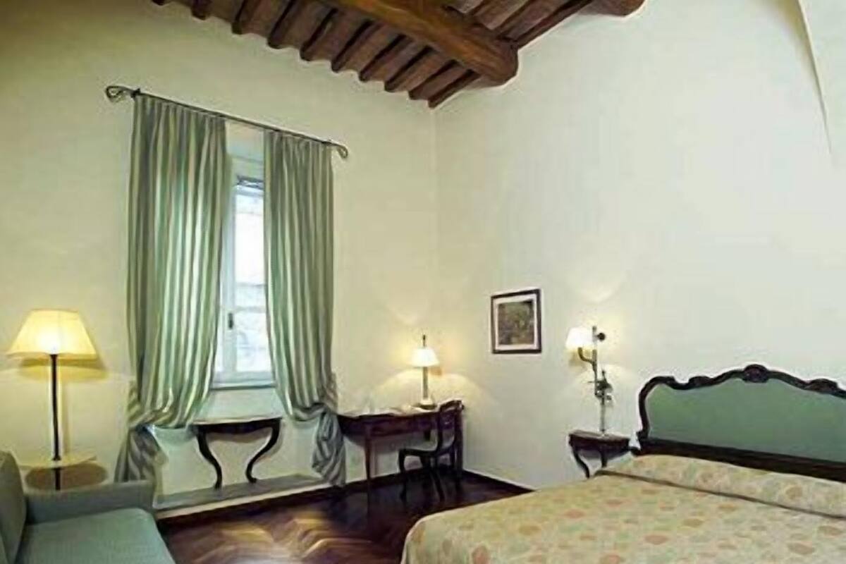 A bedroom with a bed, a chair, a desk, and a window with curtains.