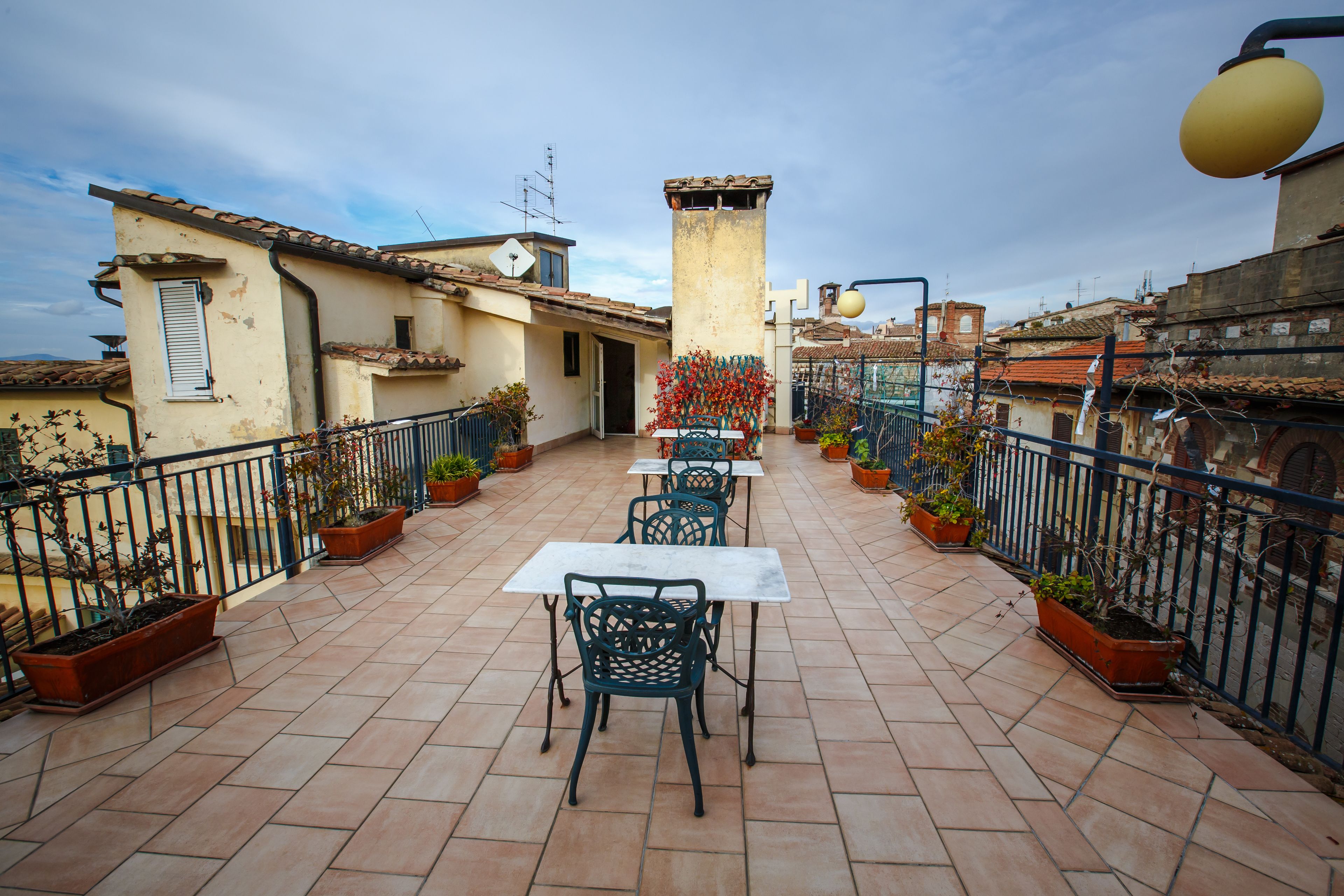 A rooftop terrace with outdoor seating, potted plants, and a view of the cityscape.