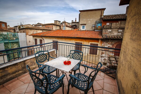 Un balcón con mesa y sillas, con vistas a un paisaje urbano de tejados de terracota y edificios históricos.