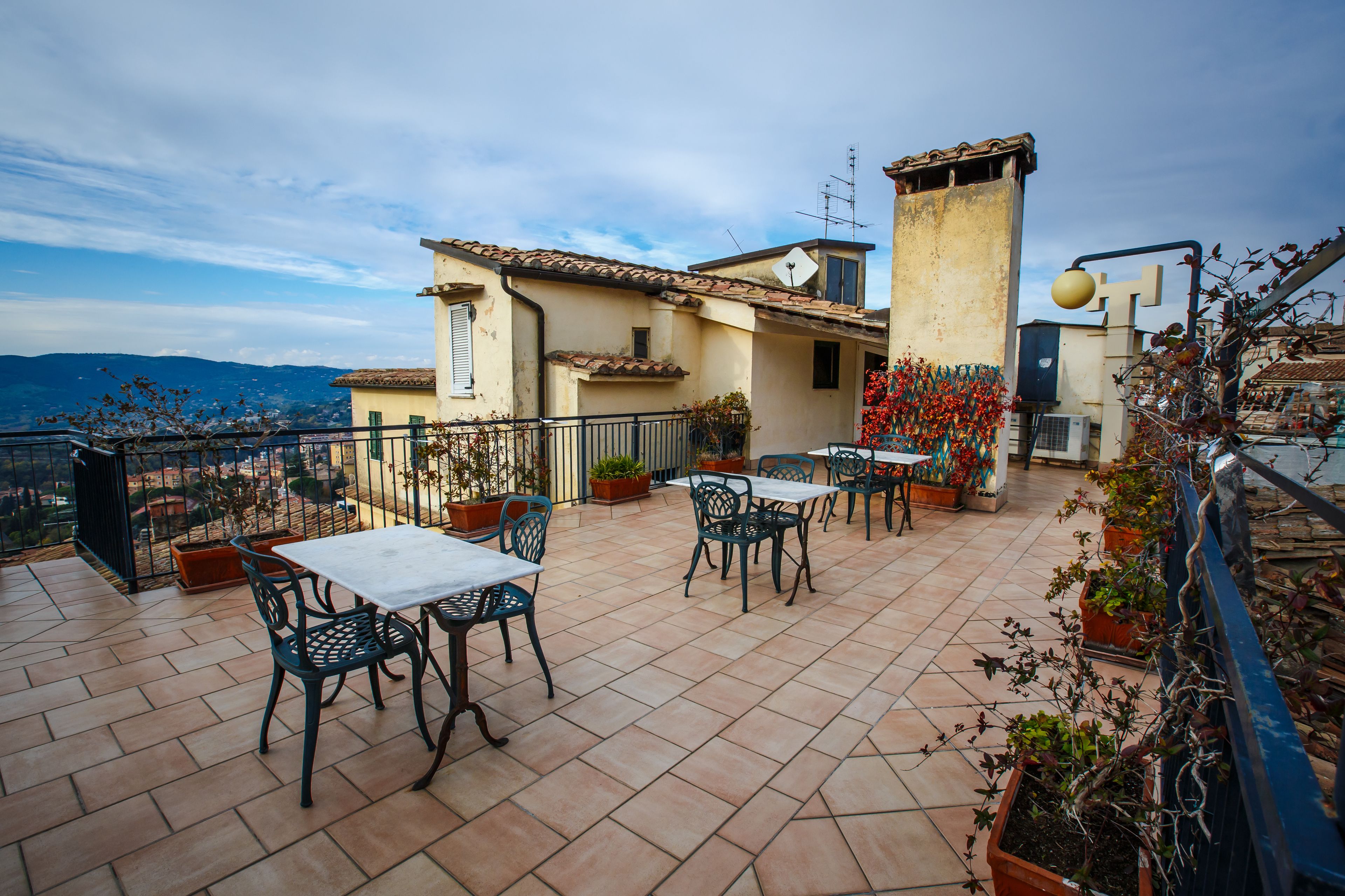 A rooftop terrace with outdoor seating, potted plants, and a view of the cityscape.