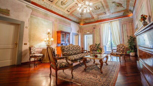 A room with ornate ceiling artwork, a chandelier, and floral-patterned furniture. - Hotel Fortuna (Perugia)