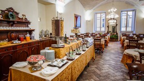 A banquet hall with long tables, a buffet with various food items, and a chandelier. - Hotel Fortuna (Perugia)