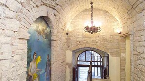 A stone-walled hallway with a mural, a chandelier, and a wooden staircase. - Hotel Fortuna (Perugia)