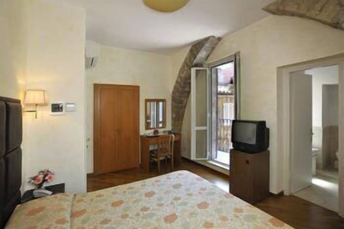 A bedroom with a bed, a desk, a television, and a window.