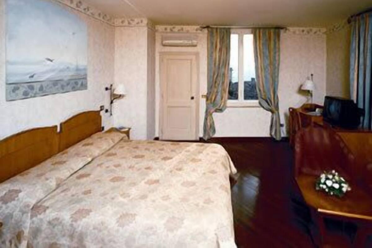 A hotel room with a bed, a desk, a chair, a television, and a window with curtains.