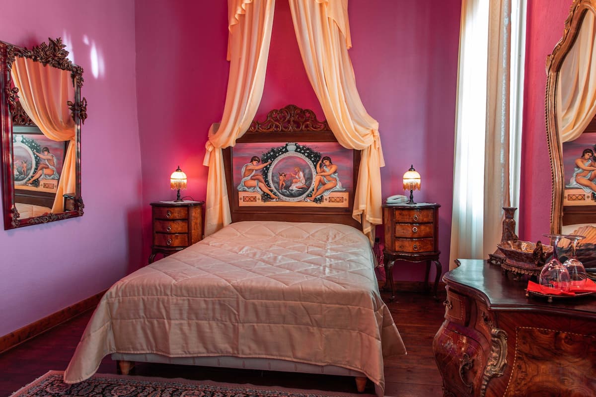 Un dormitorio con cama con dosel, cabecera ornamentada y dos mesitas de noche con lámparas.