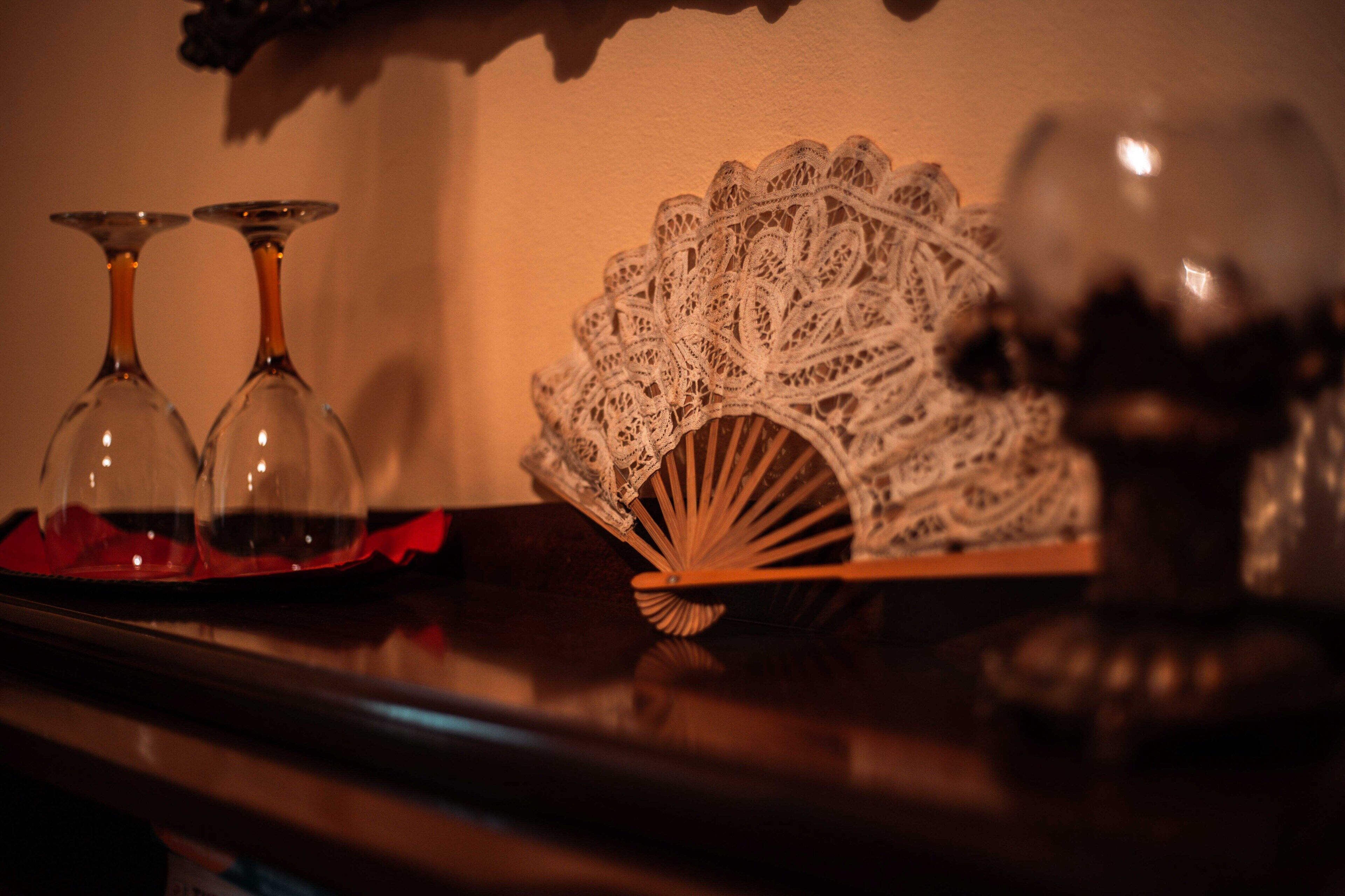 A table with two clear wine glasses, a lace fan, and a decorative vase.