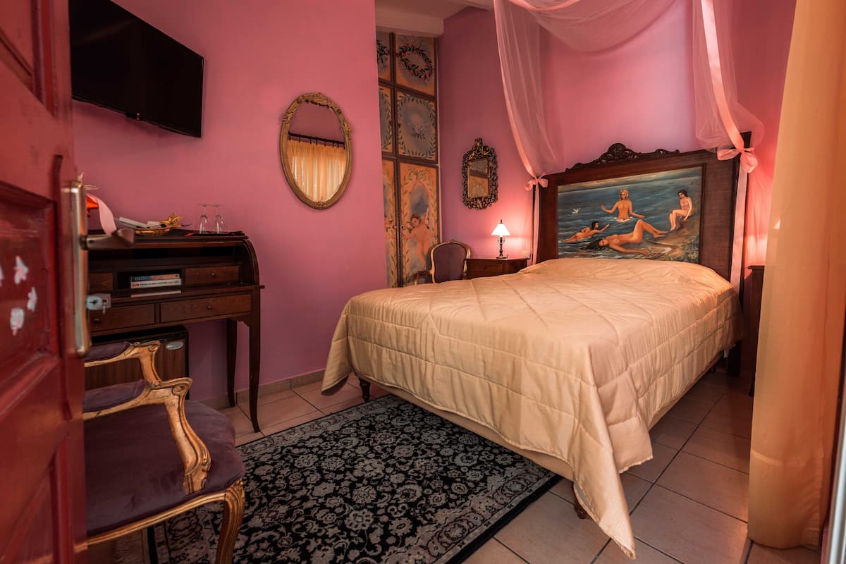 Un dormitorio con cama, escritorio, silla, televisor y un cuadro en la pared.