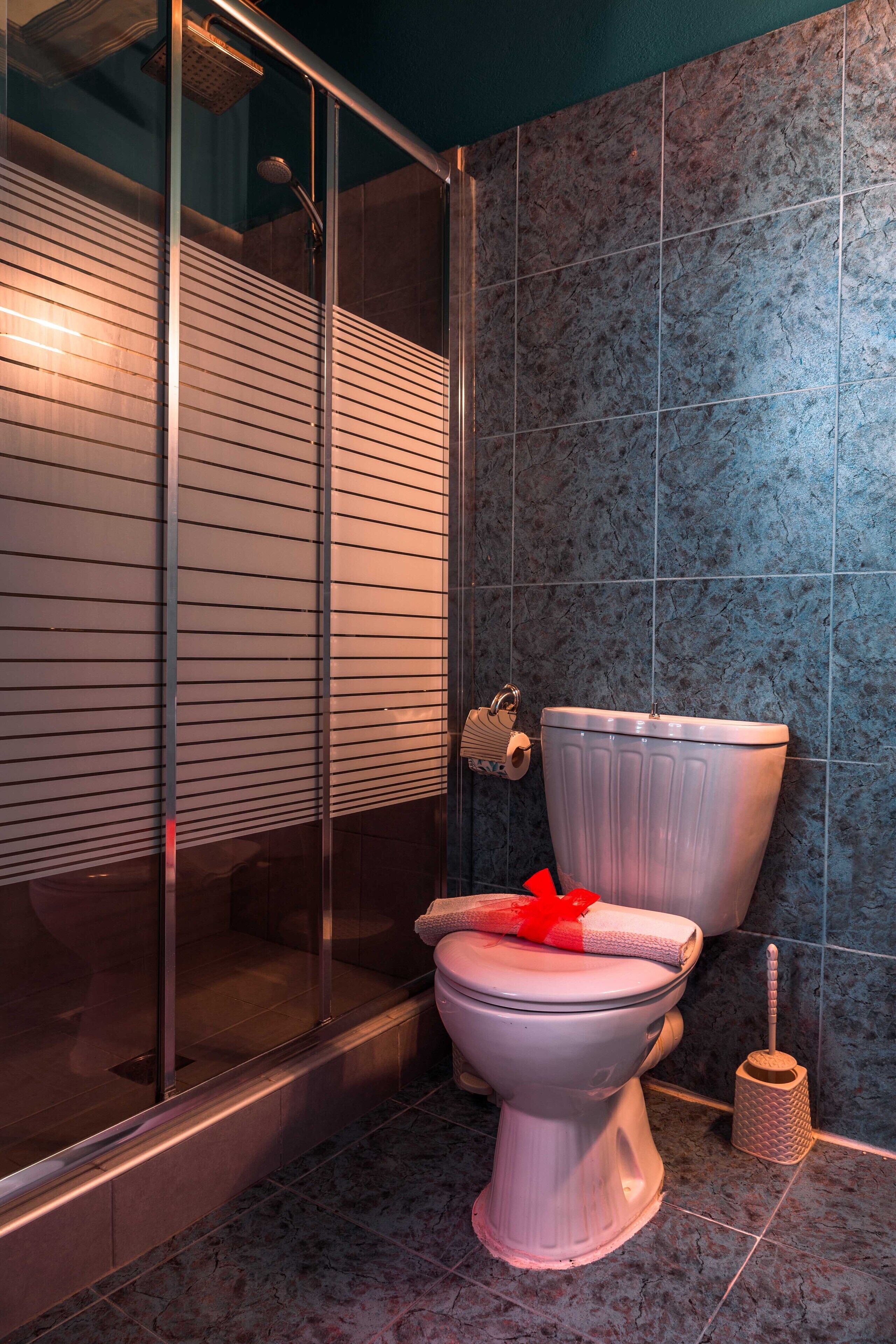 A modern bathroom with a glass shower enclosure, a white toilet, and a marble-tiled wall.