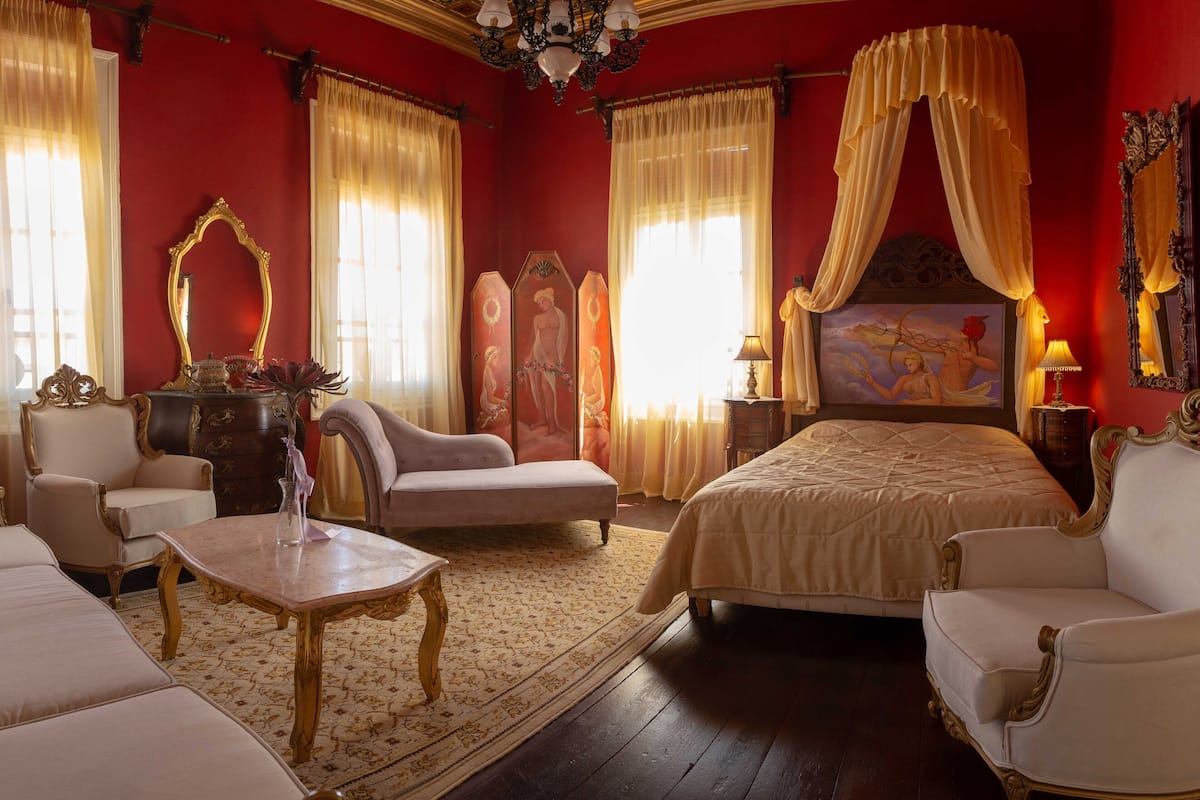 Un dormitorio lujoso con una cama grande, dos sillones, una mesita y una araña.