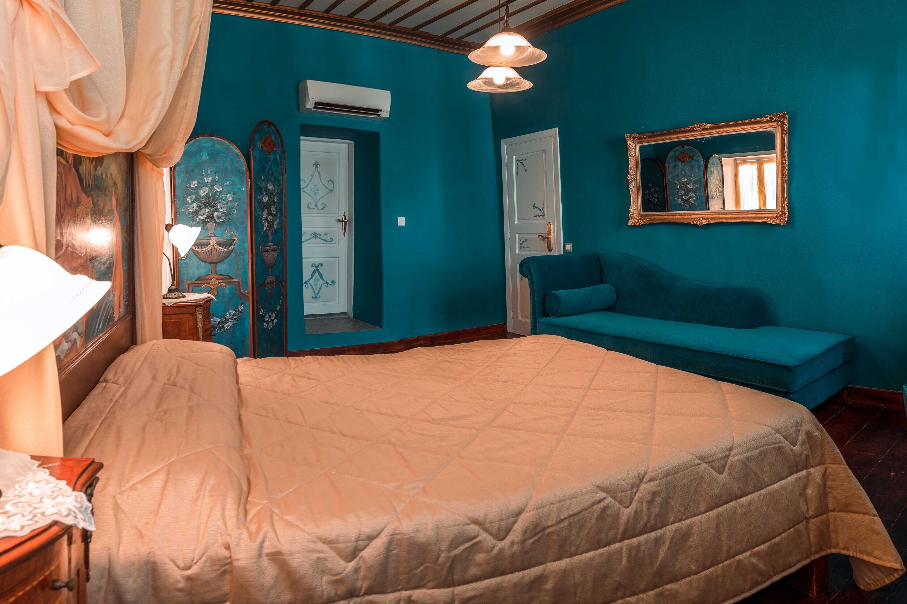Une chambre avec un grand lit, un canapé bleu et un miroir au mur.