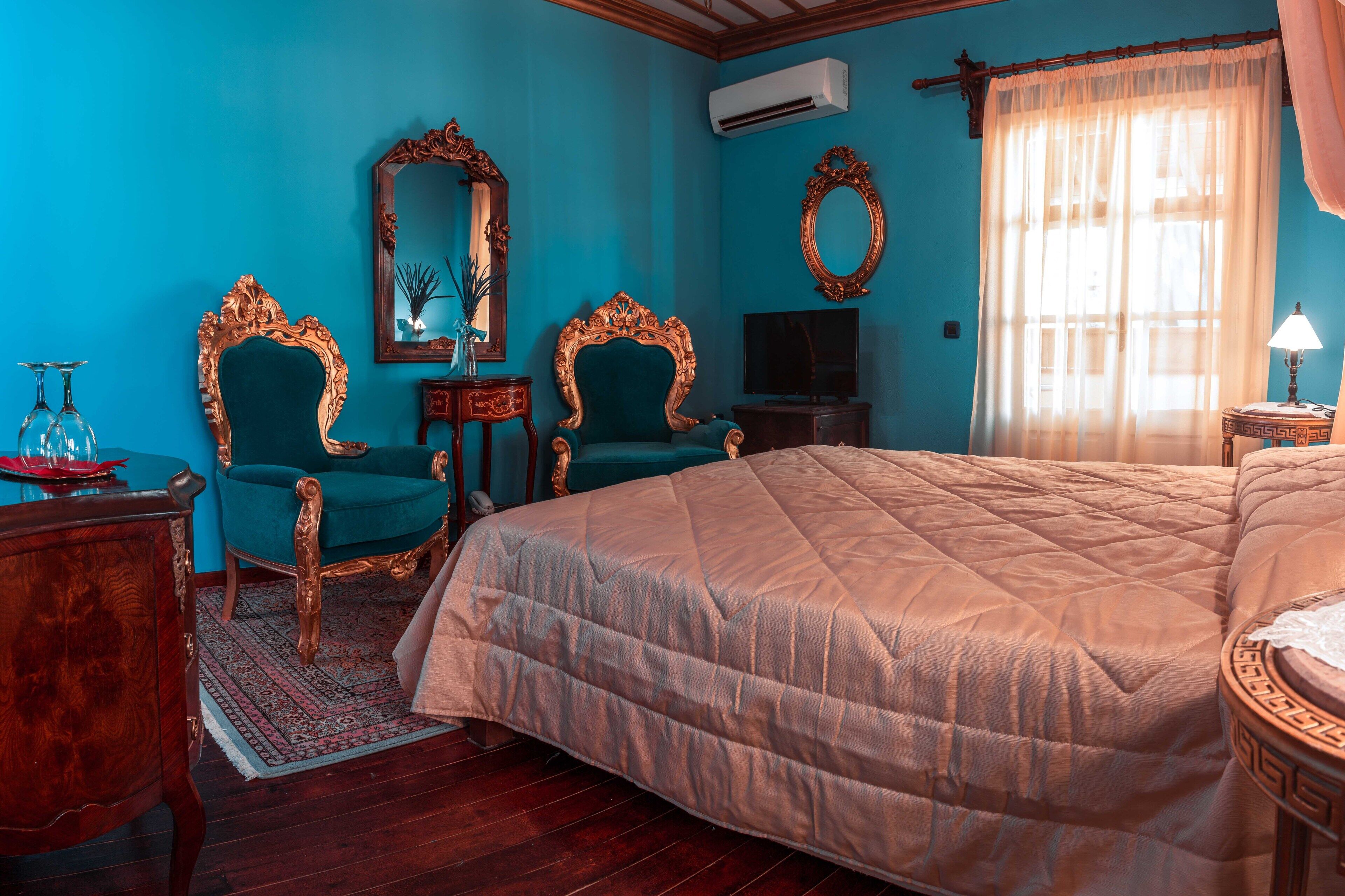 Una stanza con un letto grande, due poltrone decorate, una televisione e uno specchio.