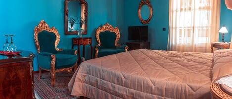 Una habitación con una cama grande, dos sillones decorados, un televisor y un espejo.