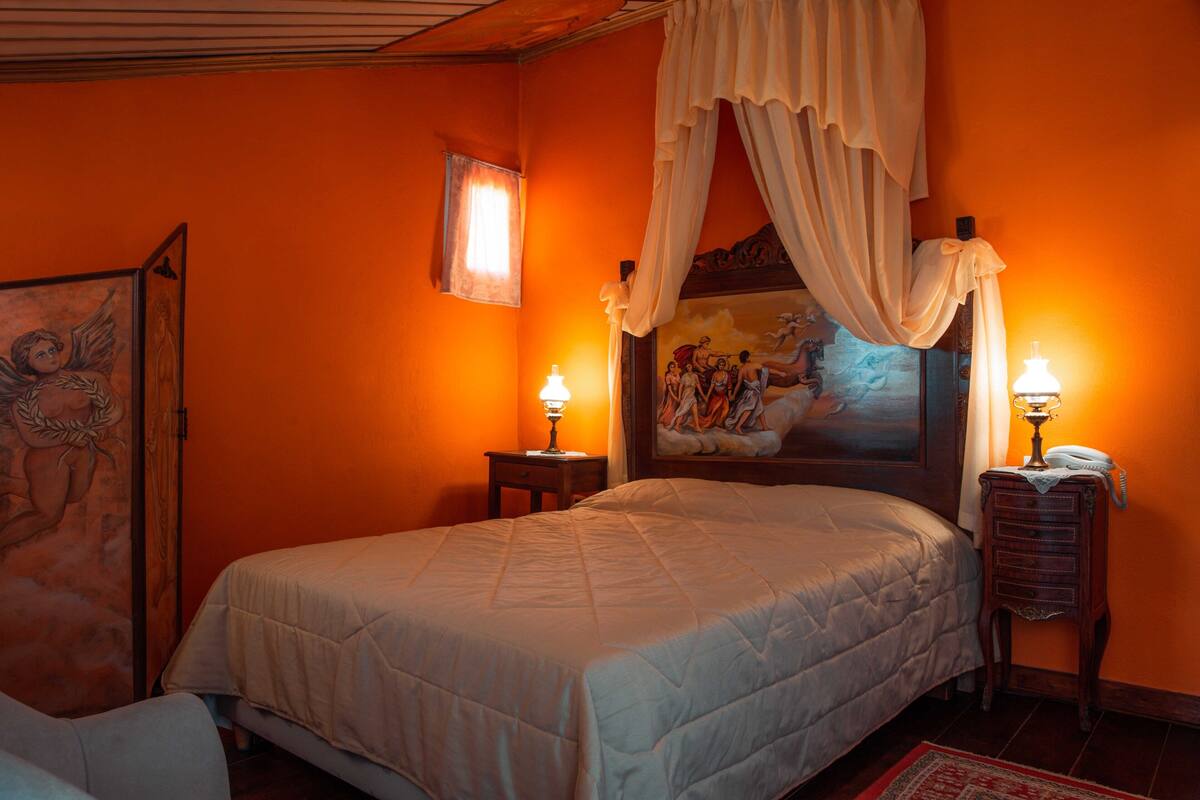 Un dormitorio con una cama, dos lámparas de noche, una mesita de noche, un cuadro y una ventana con cortinas.