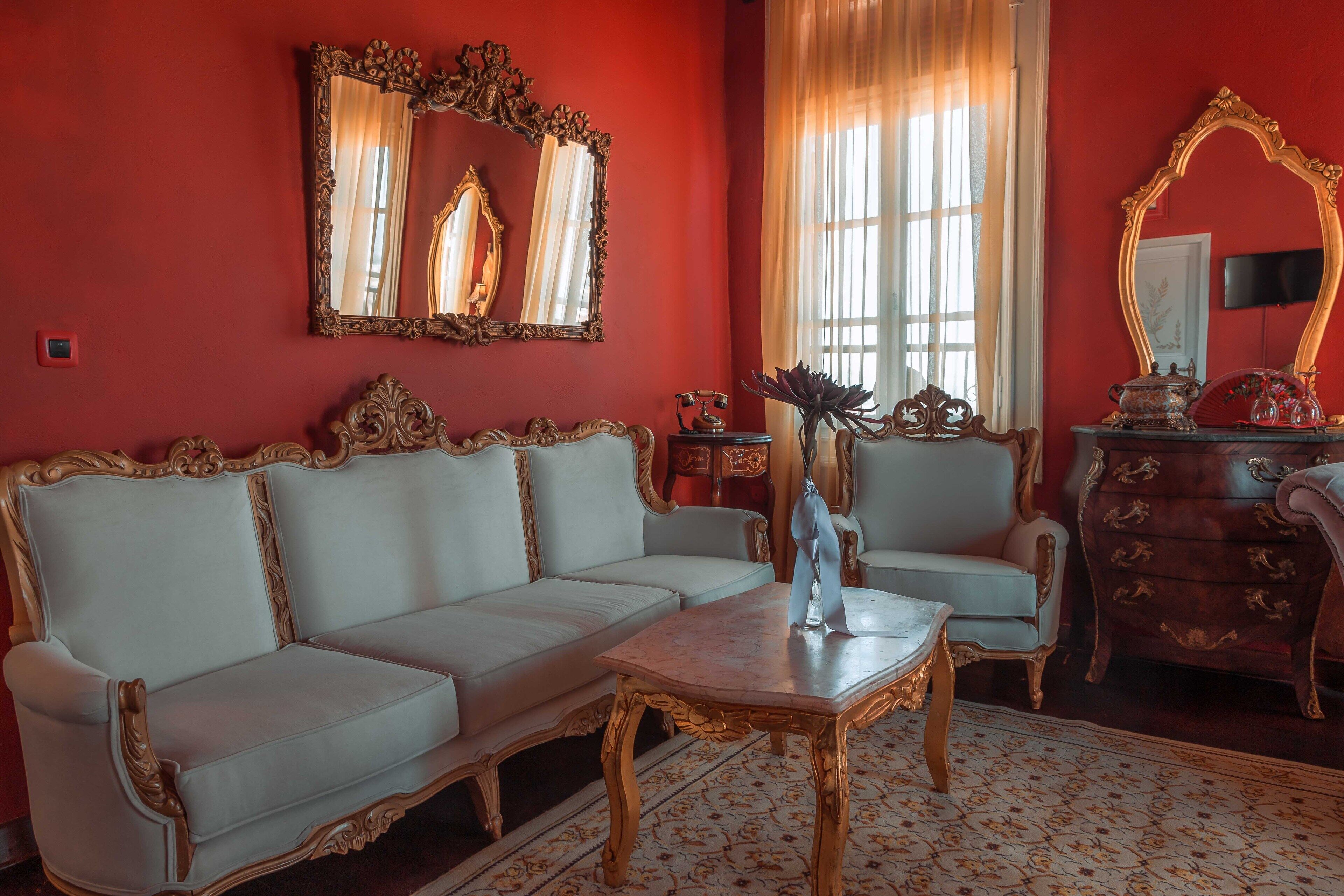 A room with a red wall, a white sofa, a wooden coffee table, a side table, and a mirror with an ornate frame.