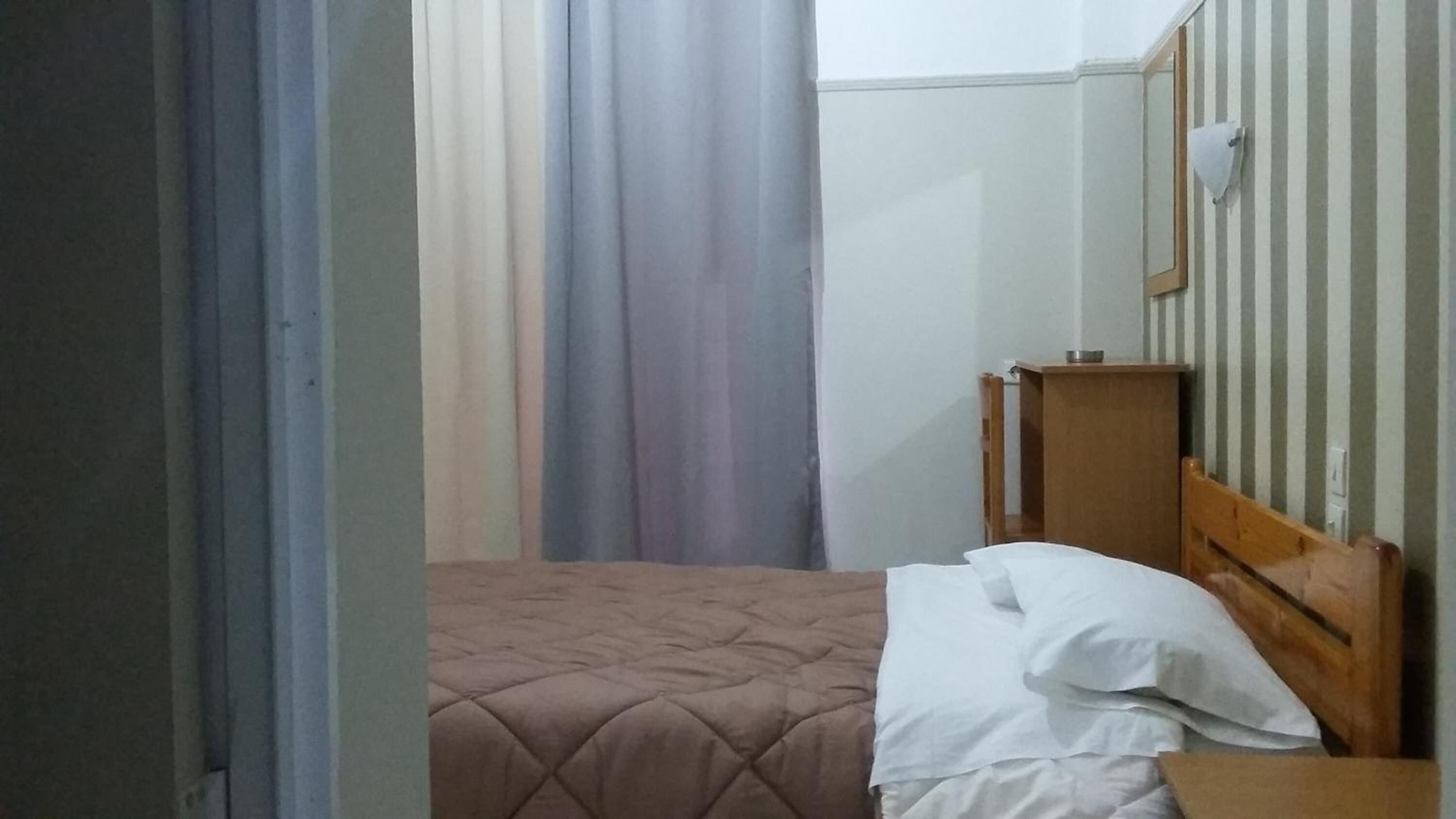 A small, simple room with a bed, a wooden headboard, and a nightstand.