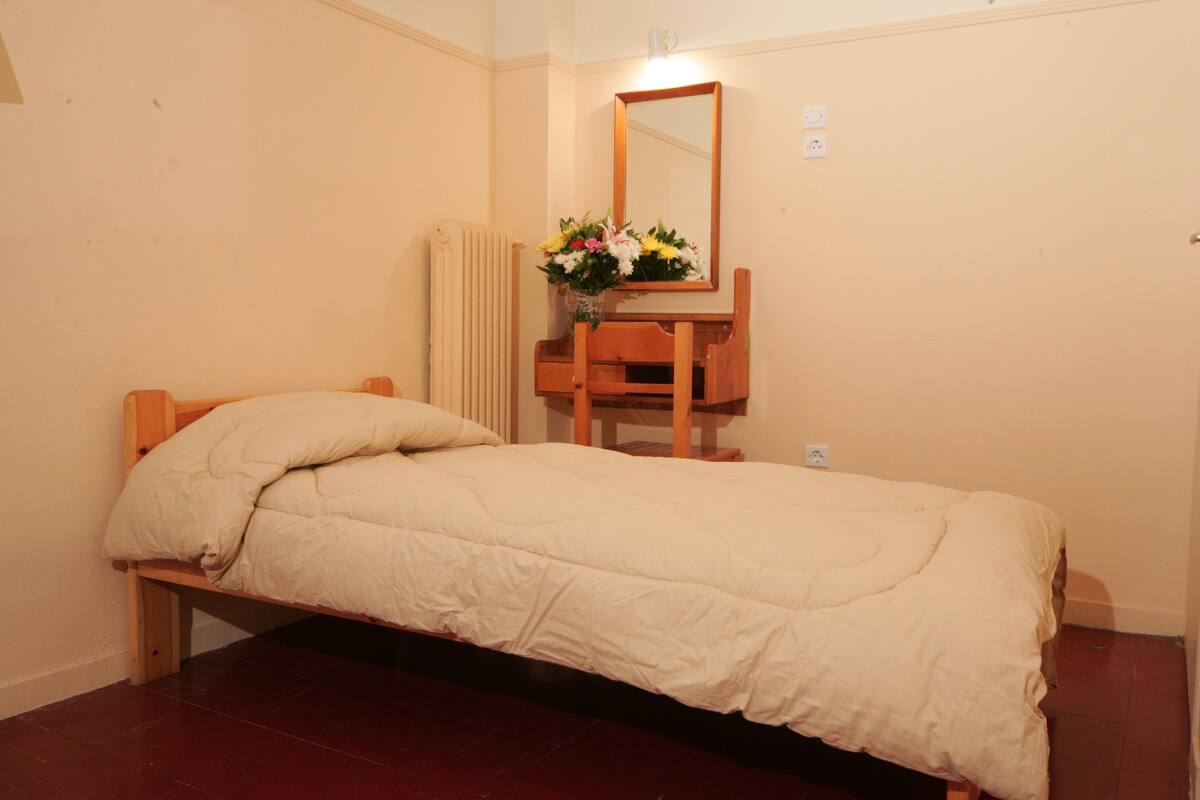 A small, single-bed room with a wooden bed frame, a bedside table, and a mirror above it.