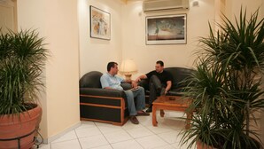 A room with two black leather sofas, a wooden coffee table, and potted plants. - Alma Hotel (Athens)