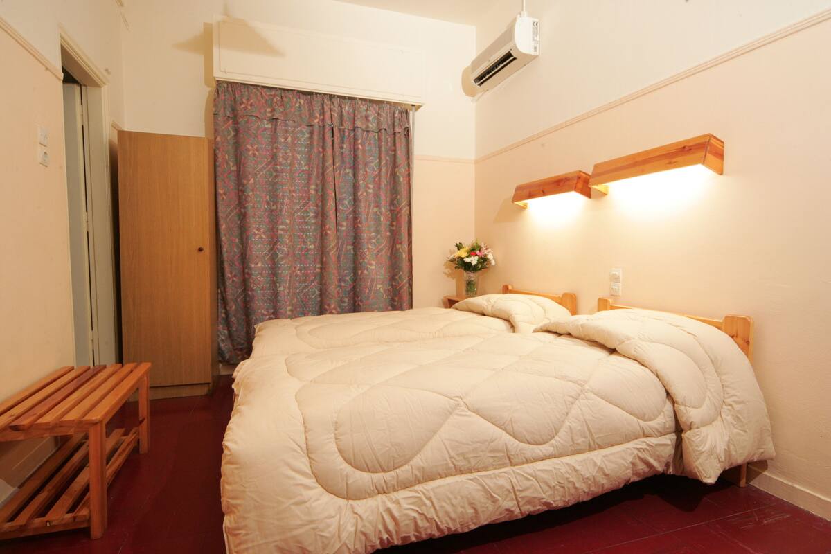 A bedroom with a bed, a wooden bench, a wardrobe, a curtain, and a wall-mounted light fixture.