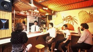 A bar area with wooden stools, a counter, and a mural on the wall. - Alma Hotel (Athens)
