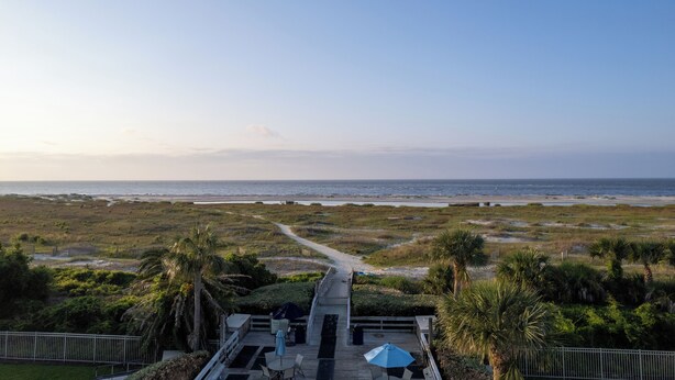 A beach view from a deck with a pathway leading to the shore, surrounded by palm trees and a fence. - Hodnett Cooper's Beach Club (St. Simons Island)