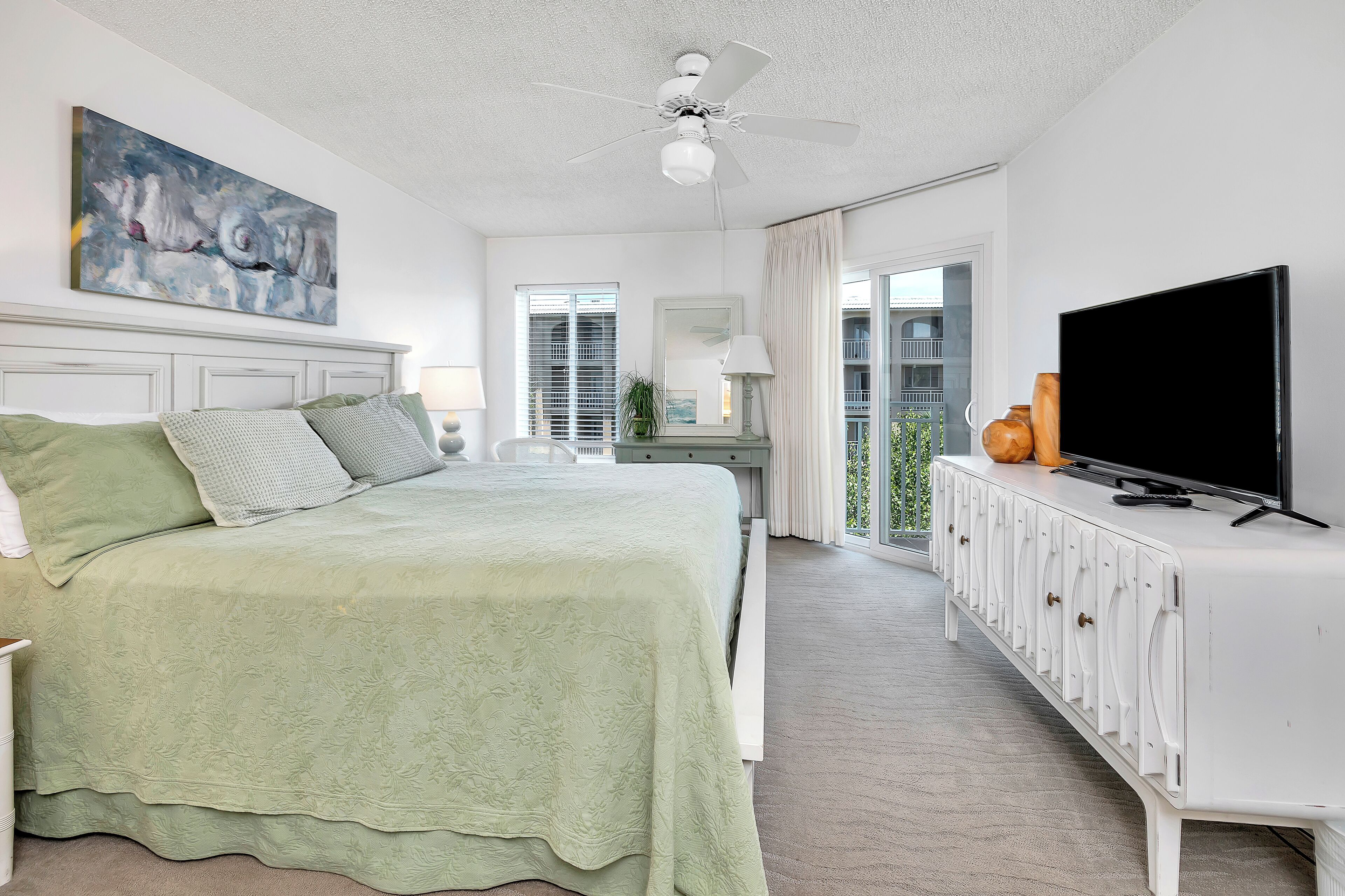 Ein Schlafzimmer mit Bett, Fernseher, Deckenventilator und einem Balkon mit Blick.