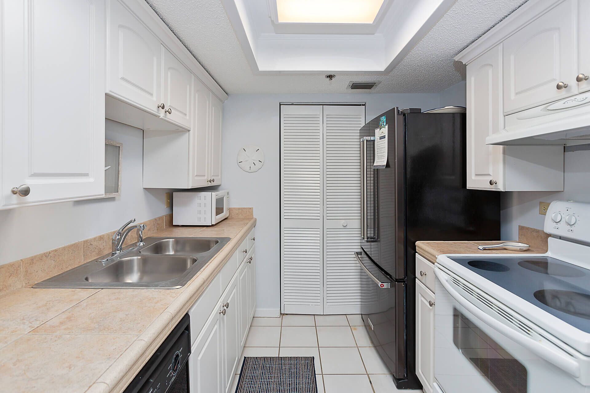 A compact kitchen with white cabinets, a stainless steel sink, a microwave, a refrigerator, and an oven.