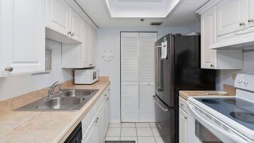 A compact kitchen with white cabinets, a stainless steel sink, a microwave, a refrigerator, and an oven.