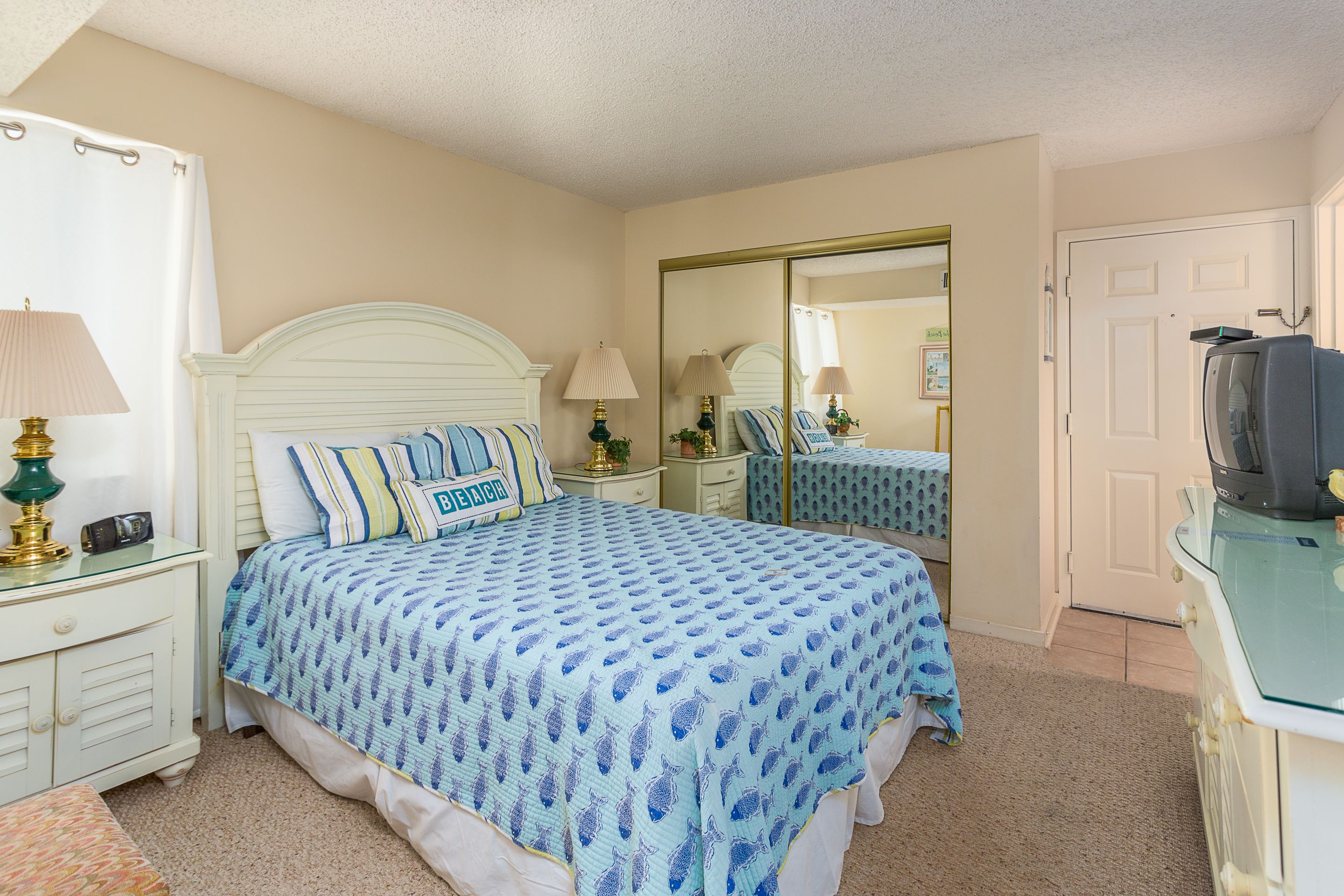 A bedroom with a bed, bedside tables, a dresser, a mirror, and a television.