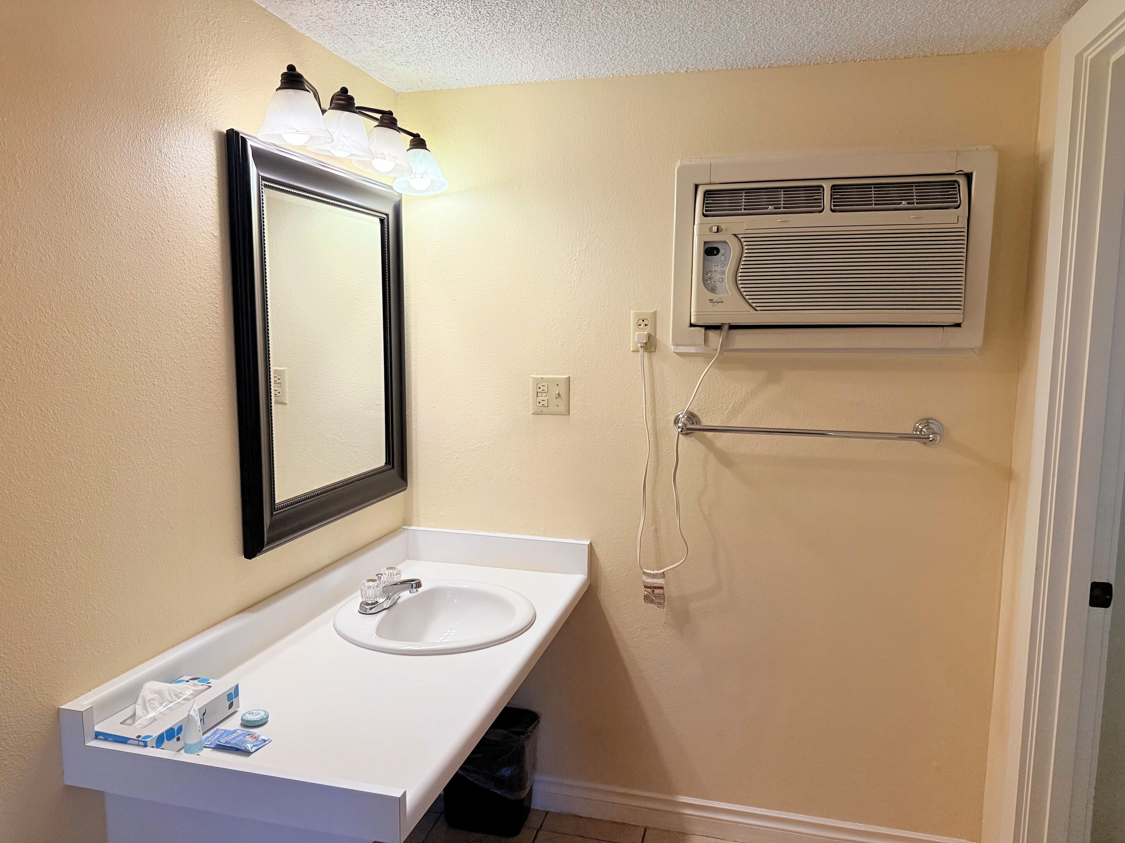 A bathroom with a white sink, a mirror with lights, and a wall-mounted air conditioner.
