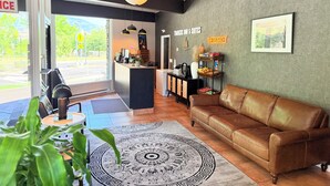 A modern hotel lobby with a leather sofa, a coffee table, a patterned rug, a reception desk, and a wall-mounted snack station. - Timbers INN and Suites (Ashland)