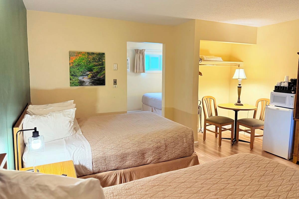 A hotel room with a bed, a desk, a chair, a lamp, and a refrigerator.