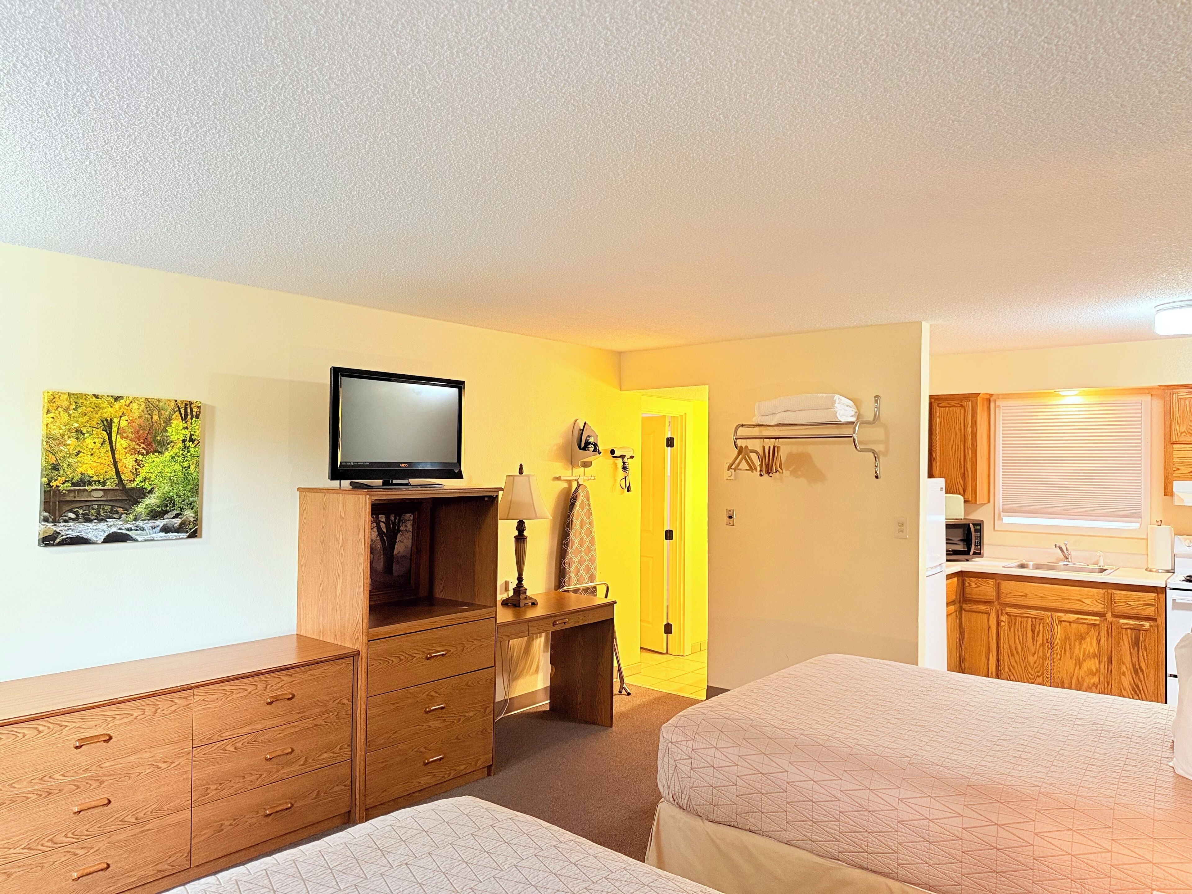Een hotelkamer met twee bedden, een houten dressoir, een televisie, een schilderij, een bureau en een kitchenette.