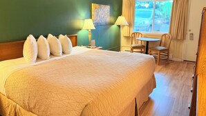 A hotel room with a large bed, a desk, and a window with curtains. - Timbers INN and Suites (Ashland)
