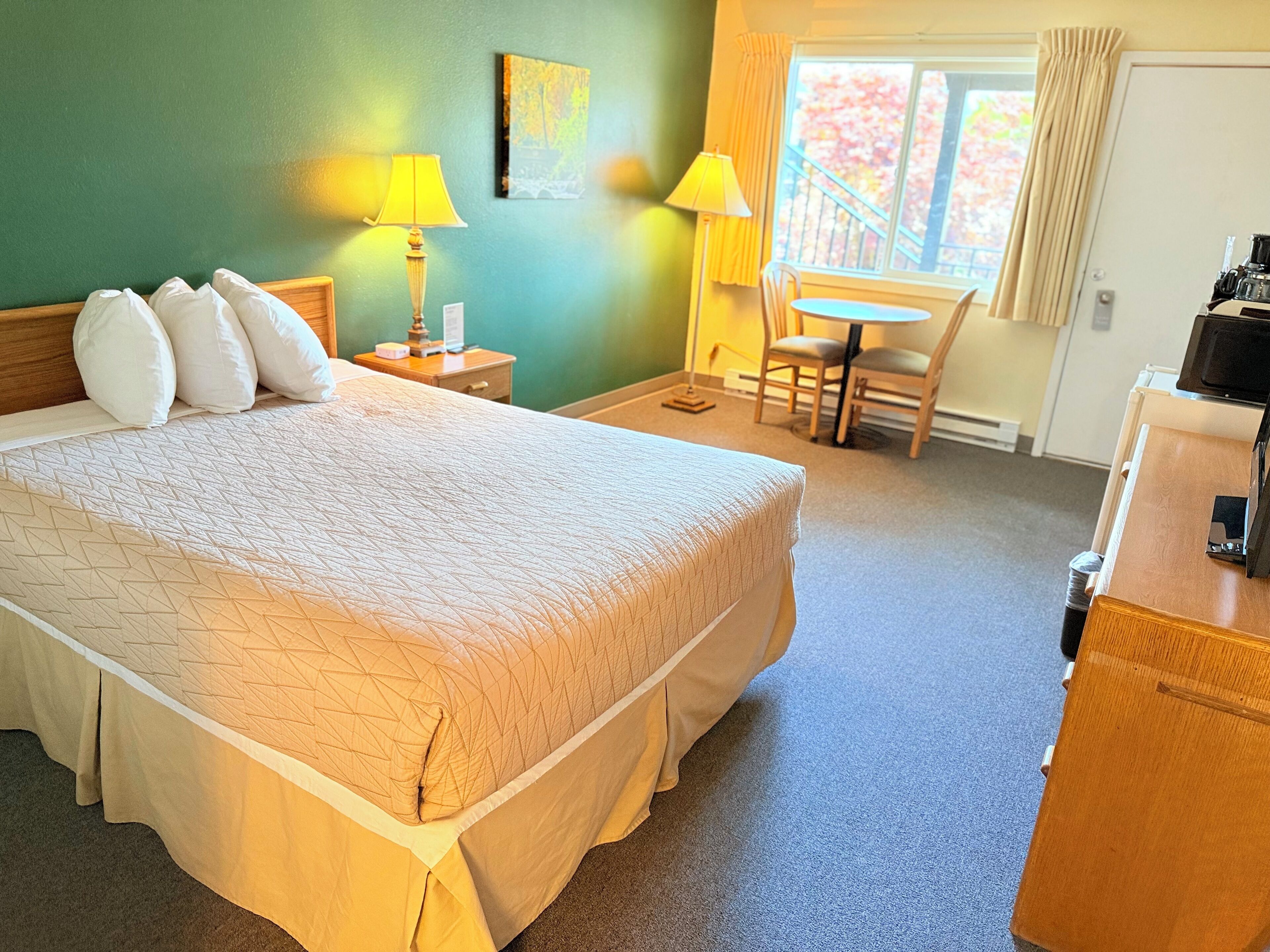 Una habitación de hotel con una cama grande, un escritorio, una silla y una ventana con cortinas.