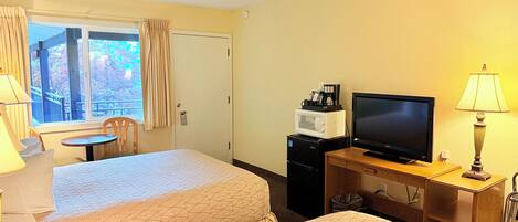 Habitación de hotel con dos camas, televisor, cafetera y escritorio con lámpara.