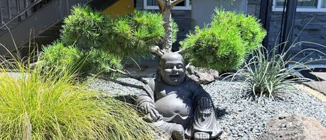 Un jardín zen con una estatua, rodeado de diversas plantas y rocas.