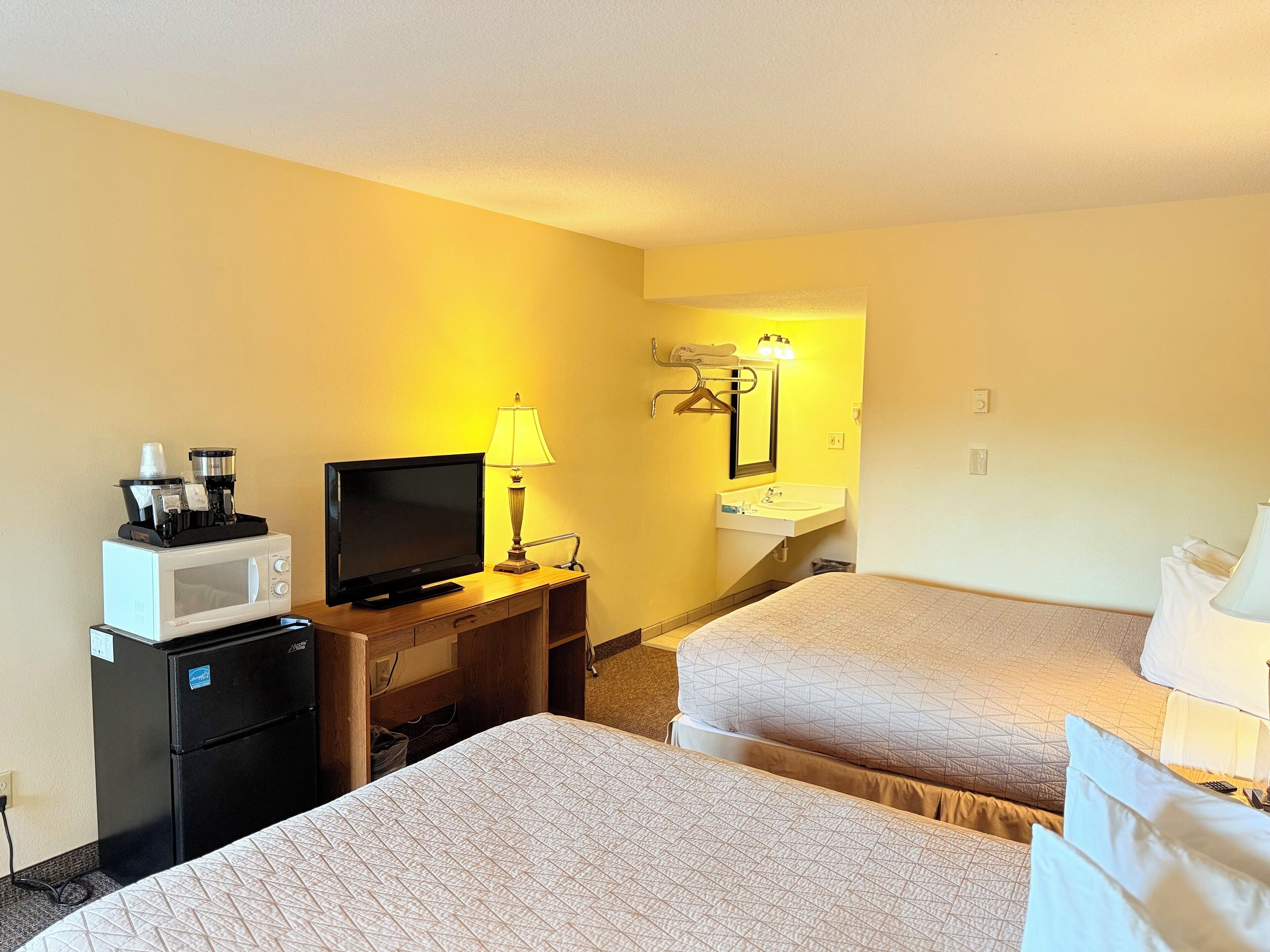 A hotel room with two beds, a TV, a microwave, a coffee maker, and a sink.