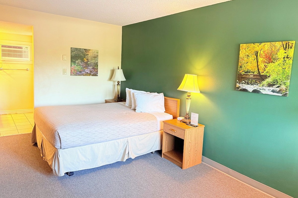 A hotel room with a bed, bedside tables, a lamp, and two paintings on the wall.